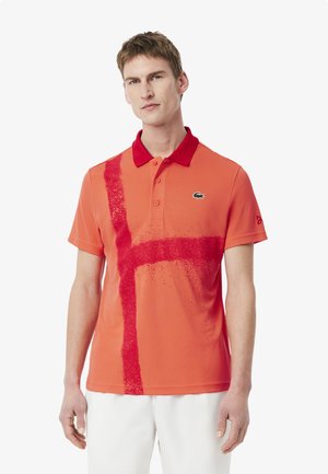 Röd polo tröja med ett kontrasterande röd randdesign, en knäppbar krage och en liten logotyp på bröstet. Tillverkad av ett mjukt, andningsbart material.