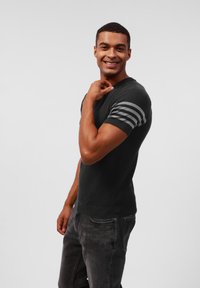 Mørkegrå ribbet t-skjorte med kort erme, med svarte og grå striper på ermene, sammen med grå jeans.