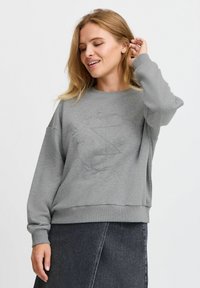 Sudadera gris con un diseño texturizado en la parte delantera, puños y dobladillo acanalados. Combinada con una falda de mezclilla oscura. Tejido suave y casual.