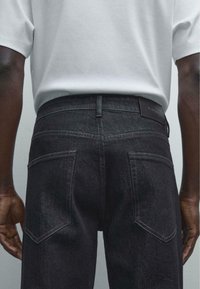 Black denim jeans with a straight leg, visible stitching on pockets, and a leather logo patch on the waistband. Simple and functional design.