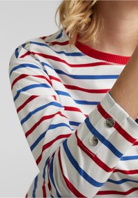 Camicia a maniche lunghe a righe con linee rosse e blu su sfondo bianco, scollo rotondo e dettagli a scatto sui polsini.
