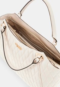 Borsa a tracolla trapuntata crema con hardware dorato, doppio manico e zip aperta che rivela slot per carte all'interno e fodera in tessuto con logo del marchio.