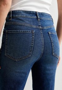 Högmidjade mörkblå jeans med en mjuk textur, med två bakfickor och kontrasterande sömmar längs kanten.