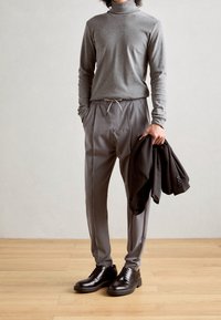Grauer langärmeliger Rollkragenpullover, gestreifte graue Hose mit Kordelzug und schwarze Lederschuhe, hält ein schwarzes Blazer. Minimalistisches Design.