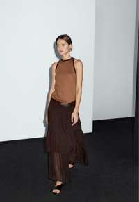 Brown tank top with contrasting straps, paired with a layered brown skirt. The outfit features a wide belt with a silver buckle and open-toed shoes.