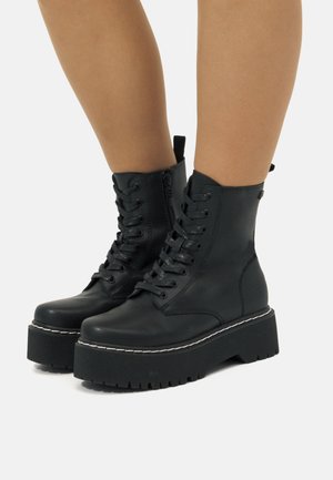 Bottines noires en cuir avec un laçage sur le devant, semelles compensées et fermeture zippée sur le côté. Couture contrastante le long de la semelle et semelle en caoutchouc texturé.