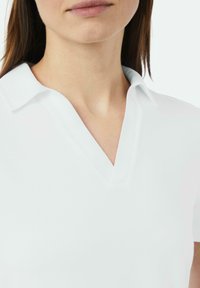 Weißes Polohemd mit V-Ausschnitt-Design, das eine weiche Textur und einen lässigen Kragen aufweist. Saubere Linien, minimalistischer Stil und keine sichtbare Markenkennzeichnung.