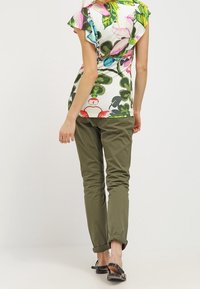 Top de manga corta con estampado floral en blanco, que presenta hojas verdes y flores rosas, combinado con pantalones ajustados verde oliva y sandalias negras.