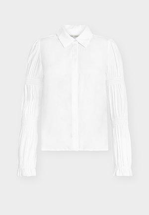 Blusa branca com design de botões, apresentando mangas compridas com detalhes franzidos. Tecido liso e gola clássica.