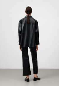 Camicia in ecopelle nera abbinata a pantaloni coordinati. La camicia ha un colletto e una vestibilità morbida; i pantaloni presentano un design con gamba dritta.