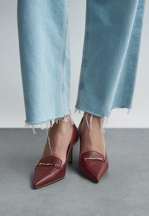 Red leather high-heeled pumps with a pointed toe, featuring a gold accent. Paired with light blue frayed hem jeans.