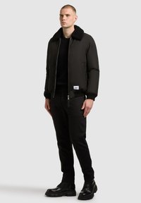 Czarna kurtka bomberka z futrzanym kołnierzem, zestawiona z czarnym swetrem i spodniami. Dopełnieniem stroju są błyszczące czarne buty. Prosty, nowoczesny design.