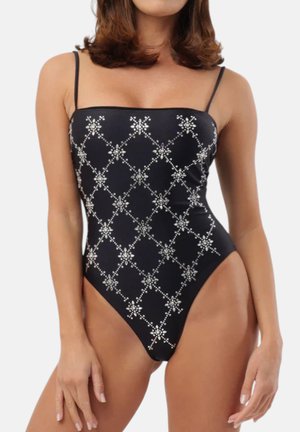 Donna che indossa un costume intero nero con spalline sottili e motivo a rete floreale argentata sul davanti.