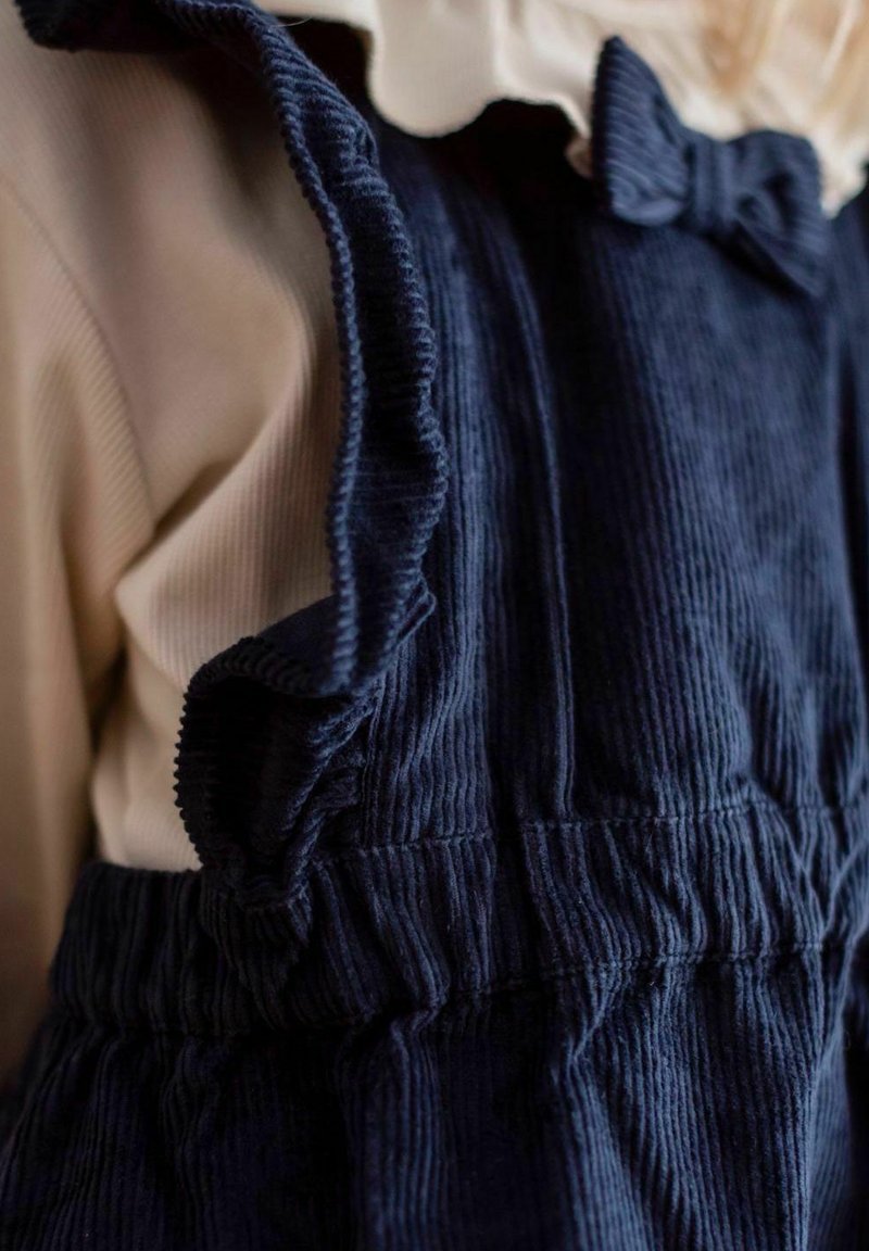 Marinvärgad korduroy overall med volangkanter, kombinerad med en ljusbeige långärmad topp med mjukt material. Slipsdetalj på overallen.