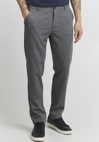 Gray trousers in a smooth, textured fabric with side pockets, a button closure, and contrasting trim. Paired with black sneakers.