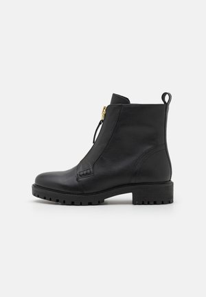 Bottine en cuir noir avec bout rond, fermeture éclair latérale et détail texturé. Dotée d'une semelle épaisse et texturée ainsi que d'une petite languette de tirage.