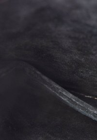 Gros plan d’un tissu noir doux avec un pli, montrant la texture et un léger éclat à la surface.