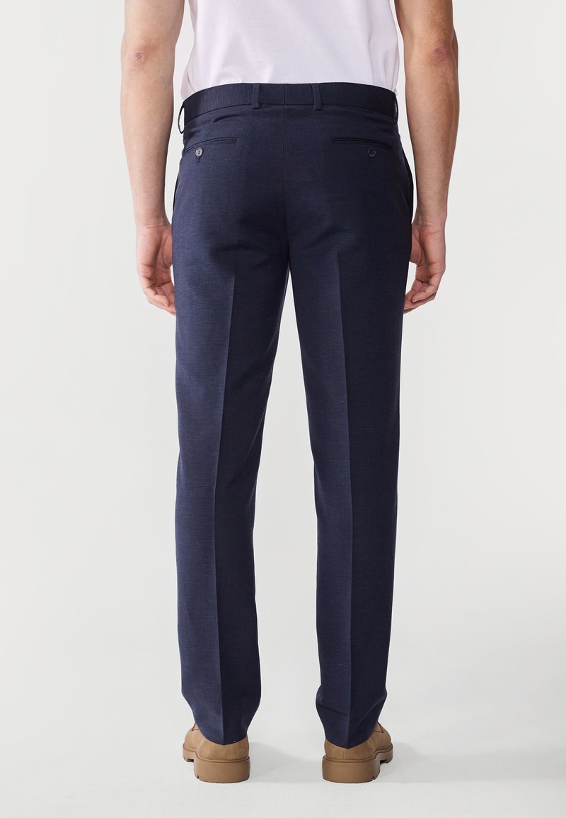 Pantalons de costume navy en tissu texturé, dotés de poches arrière doubles, d'une coupe droite et d'une taille fine. Associés à des chaussures marron clair.