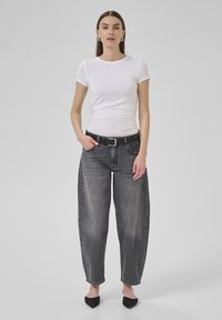 T-shirt blanc ajusté à manches courtes, associé à un jean en denim gris ample taille haute et une ceinture noire. Ballets noirs à bout pointu.