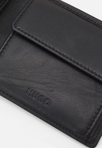 Black leather cardholder with textured surface, featuring a front flap pocket and embossed "HUGO" logo. Stitched edges enhance durability.