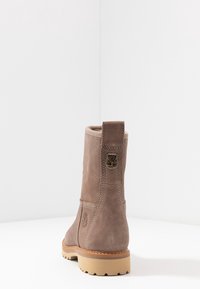 Taupe Wildleder-Ankle-Boot mit dicker beiger Sohle, Rückenzugschlaufe, genähten Details und geprägtem Baum-Logo an der Seite.
