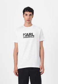 Hvit bomullst-skjorte med bold svart "KARL LAGERFELD"-tekst. Klassisk rund hals og korte ermer, jevn tekstur, avslappet passform.