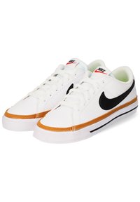 Zapatillas blancas con el swoosh negro de Nike, cuero texturizado y suela de goma, detalles en color marrón en la suela y cordones blancos.