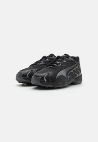 Chaussures de sport noires avec un dessus en maille, des superpositions synthétiques et une semelle en caoutchouc texturée. Les caractéristiques incluent des lacets et un design latéral en forme de flamme.