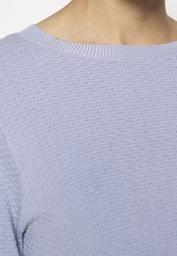Light purple knit sweater featuring a ribbed neckline and textured fabric, emphasizing softness and stretch with a relaxed fit.