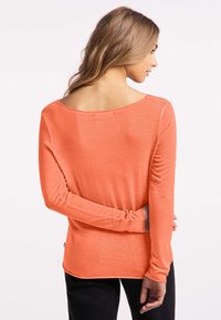 Langarmshirt in koraal, met een brede halslijn en strakke mouwen. Zachte stof met een gladde textuur, die iets over de achterkant valt.
