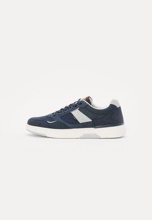 Zapatillas de ante en color marino con una suela blanca, que presentan detalles en cuero gris y una etiqueta roja y amarilla en la lengüeta; diseño con cordones.