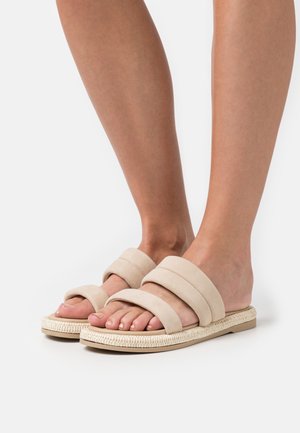 Sandales à glissière beiges avec trois larges brides en daim, une semelle en jute tissée et un design plat, mettant en avant une texture lisse et un bout ouvert.