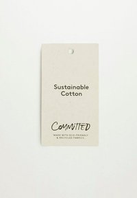 Etykieta zrównoważonej bawełny na fakturowanym, kremowym papierze. Zawiera czarny tekst z napisem „Zrównoważona bawełna” oraz „ZAANGAŻOWANI”, wraz z ekologiczną informacją.