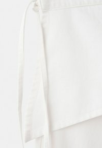 Falda cruzada de mezclilla blanca con cierre lateral de lazo y detalle de dobladillo en capas.