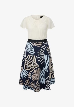 Ivory shirt met korte mouwen gecombineerd met een marineblauwe rok met beige en lichtblauwe tropische bladpatronen en een zwarte tailleband.