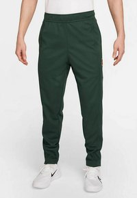 Zaļas sporta bikses, izgatavotas no mīksta, elastīga materiāla, ar sašaurinātu piegriezumu, elastīgu vidukļa jostu un sānu kabatām.