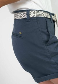 Marineblauwe shorts met een gladde textuur, voorzien van een patroonrijke witte riem, zijzakken en een gouden accent op het zakgebied.