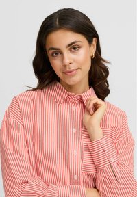 Red and white striped button-up shirt with a collar, long sleeves, and gathered cuffs, showcasing a lightweight fabric texture.