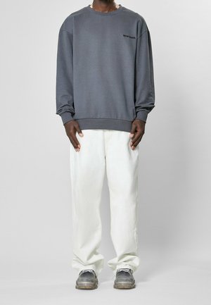 Szary sweatshirt z okrągłym dekoltem i ściągaczami, połączony z jasnymi, luźnymi spodniami. Sneakersy z przezroczystą podeszwą dopełniają outfit.