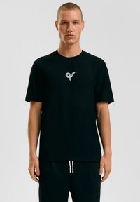 Zwart katoen T-shirt met een klein zilveren logo op de borst. Klassieke ronde hals, korte mouwen, met een relaxed fit.