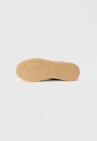 Sko sål med et tekstureret, geometrisk mønster i lyse beige gummi, der har et højt træk design og en let forhøjet kant.