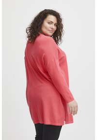 Maglione corallo a maniche lunghe, di taglio morbido, con una texture soffice, caratterizzato da un collo rotondo e spalle scese, abbinato a pantaloni neri.