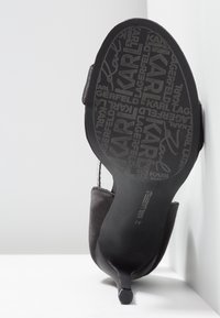 Chaussure noire à talon haut inclinée vers le haut montrant la semelle avec le texte répété du logo « Karl Lagerfeld » et le motif de la signature.