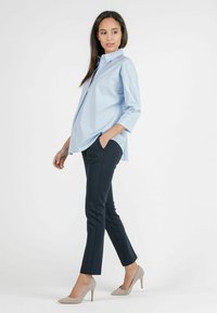 Lichtblauwe, button-up overhemd met een relaxte pasvorm en driekwartmouwen, gecombineerd met donkerblauwe slim-fit broeken en beige hakken.