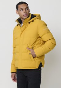 Giacca imbottita gialla con cappuccio, caratterizzata da accenti neri, tasche anteriori con zip e un logo sul colletto e sulla manica. Vestibilità regolata.