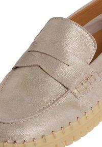 Beige semišové mokasíny s lesklým povrchem, které mají detail s penny slotem a viditelným švem, a texturovanou gumovou podrážku.