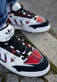 Zapatillas Adidas con parte superior de cuadros rojos y acentos en blanco y negro, suela blanca y cordones negros. Incluye detalles del logo metálico.