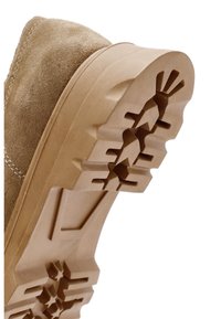 Suela de zapato de ante color marrón claro con una suela exterior de goma resistente y texturizada que presenta patrones de banda multidireccional para agarre y tracción.