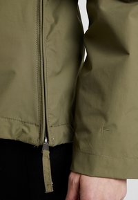 Kaki grøn jakke med en glat finish, der har en central lynlås lukning og elastiske manchetter, som viser et strømlinet design og minimal syning.