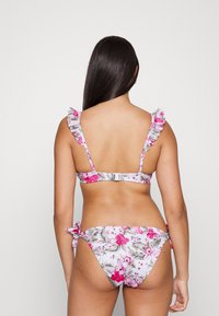 Conjunto de biquíni floral com fundo rosa claro, apresentando alças com babados, padrões tropicais e laços ajustáveis na parte inferior.